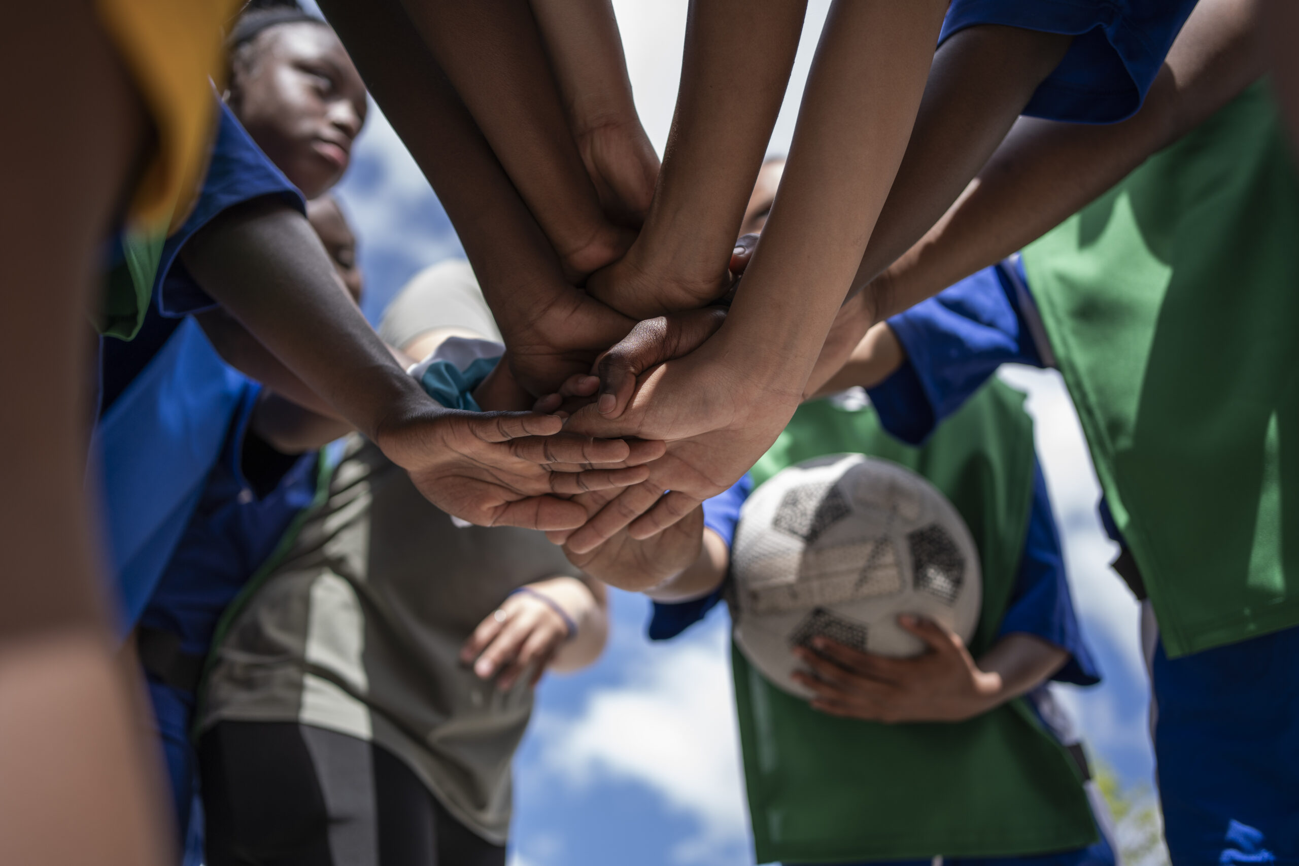 Low angle of girls soccer team standing in huddle with stacked hands before a match on the soccer field